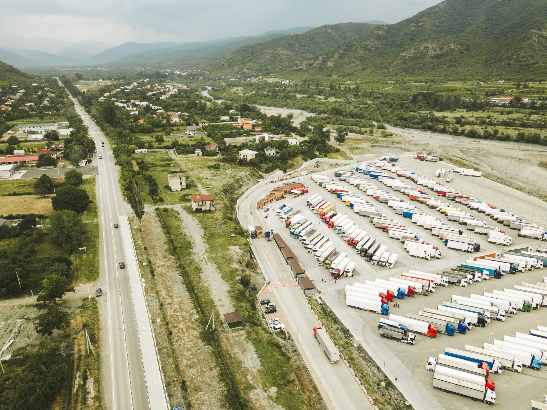 Kazbegi, Georgia - 7th july, 2024: aerial fly over lines of lorry trucks stand symmetrical in parking lot by Georgia - Russia border popular Military highway road. Caucasus import export logistics